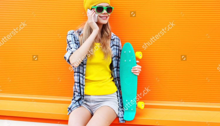 stock-photo-fashion-smiling-woman-talking-on-smartphone-with-skateboard-over-colorful-orange-background-458441089